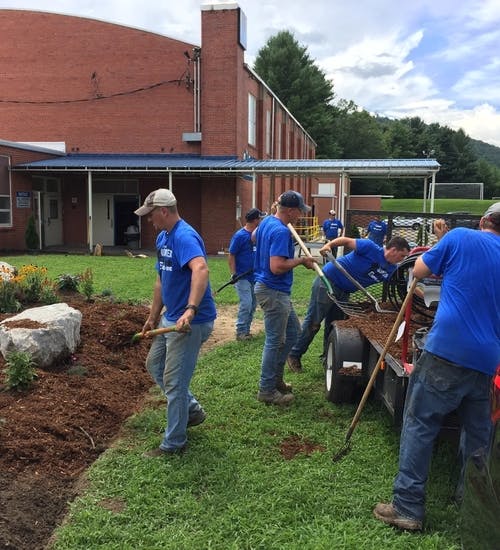 Group of people in blue shirts volunteering by landscaping a garden