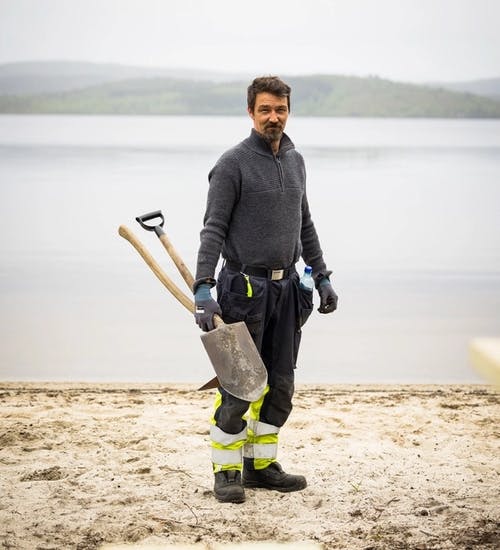 Man standing on beach in work clothes holding a shovel