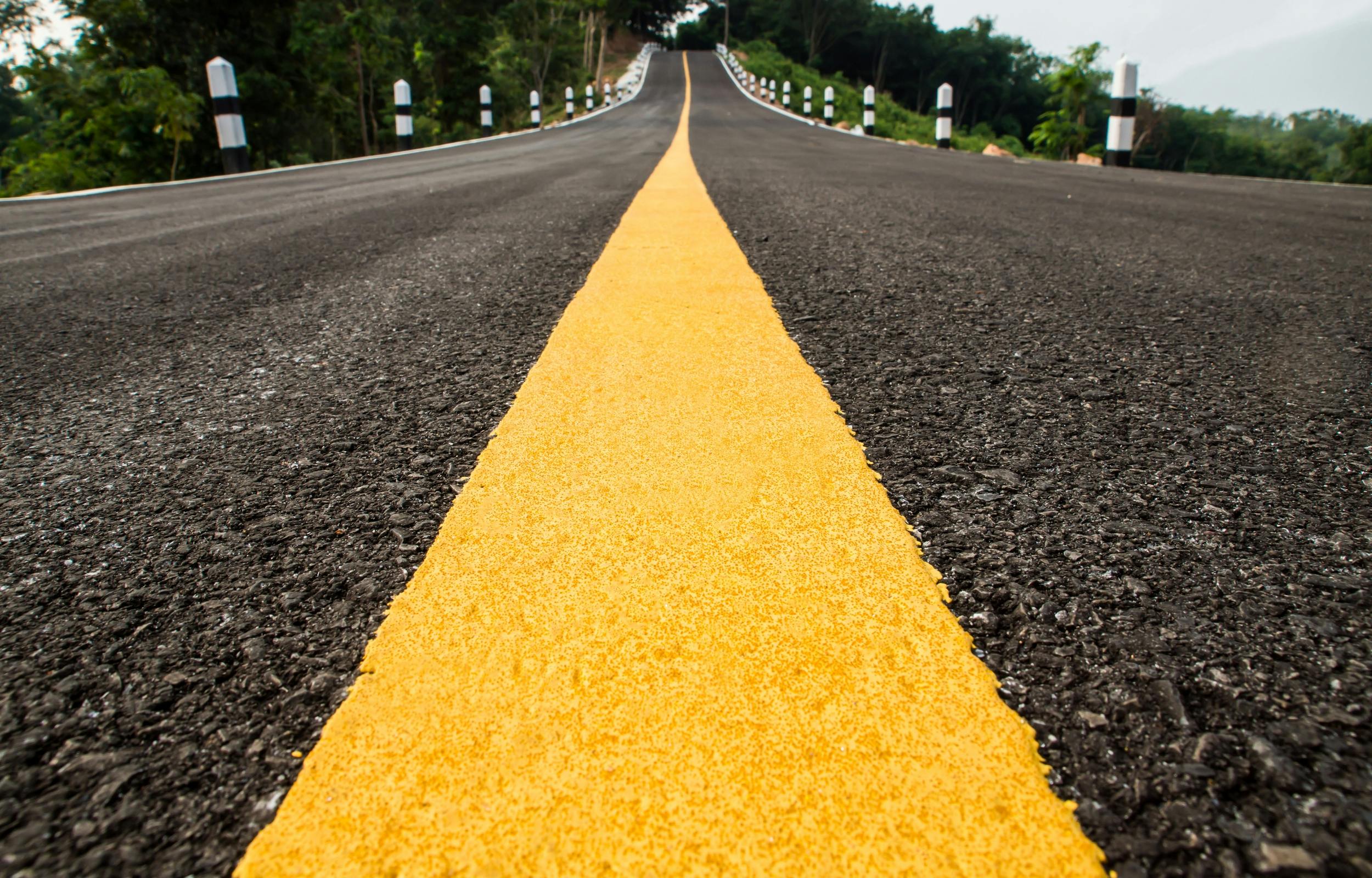 Street level view of a yellow middle line disappearing down an asphalt road into the distance.